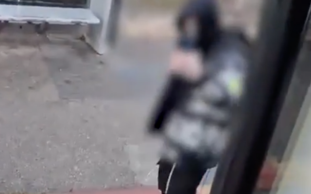 Un agresseur, portant un tsitsit, est vu en train de filmer un chauffeur de bus qui a été hospitalisé avec un bras cassé après avoir été agressé par deux personnes dans le quartier de Ramot, à Jérusalem, le 5 décembre 2025. (Crédit : Capture d'écran : Police israélienne)